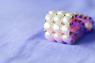 Beautiful white pearl bracelet on a purple textile background close up