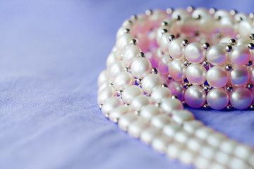Fragment of a white pearl necklace on a purple color textile background close up