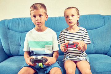 Children emotionally play a video game while sitting on the couch.
