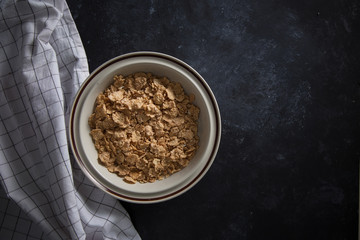 Wheat bran breakfast cereal with no milk in a bowl. Black background with homespun napkin.