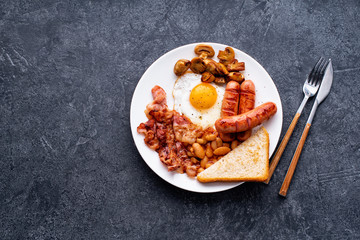 Top view flatlay with classical english breakfast with fried bacon, mushrooms and eggs. Served with black coffee.