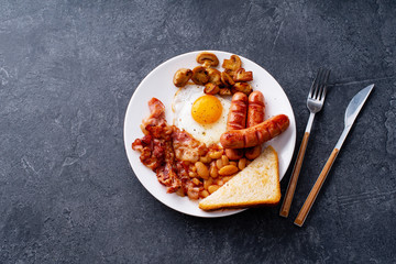 Top view flatlay with classical english breakfast with fried bacon, mushrooms and eggs. Served with black coffee.