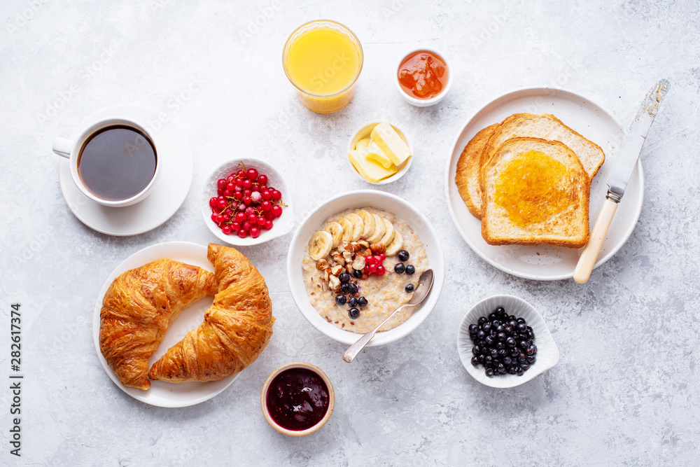 Wall mural Breakfast with oatmeal with berries and nuts, croissants, toasts with jam and butter, coffee and orange juice