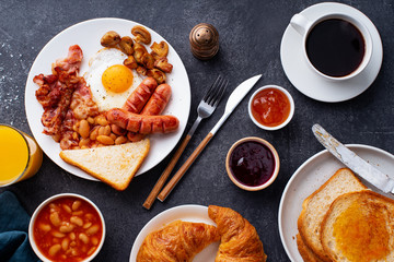 Top view flatlay with classical english breakfast with fried bacon, mushrooms and eggs. Served with orange juice, croissants and black coffee.