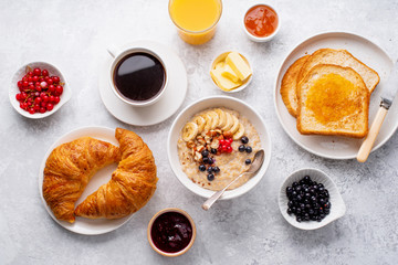 Breakfast with oatmeal with berries and nuts, croissants, toasts with jam and butter, coffee and orange juice