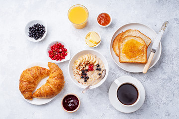 Breakfast with oatmeal with berries and nuts, croissants, toasts with jam and butter, coffee and orange juice