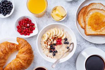 Breakfast with oatmeal with berries and nuts, croissants, toasts with jam and butter, coffee and orange juice
