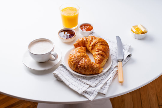 Top view flatlay with fresh croissants served with jams, coffee, orange juice and buter. Morning meal concept. White background