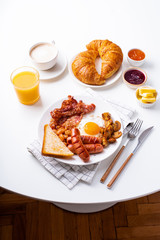 Top view flatlay with classical english breakfast with fried bacon, mushrooms and eggs. Served with orange juice, coffee and croissants. White table, cafe.