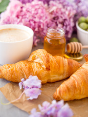 Breakfast served with coffee, croissants, natural honey jar and flowers on gray stone background. Top view.