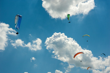 Large group of paragliders flies in the blue sky against the clouds. Paragliding on a bright sunny day.