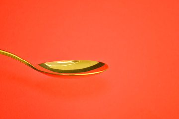 Empty golden metal spoon on a coral background, with a copyspace
