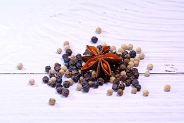 Assorted spices: Star Anise, black and white pepper on white wooden table background.