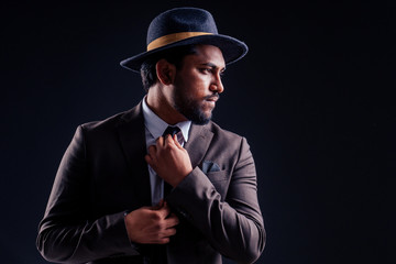 indian business man wearing hat and classic suit on black background in studio