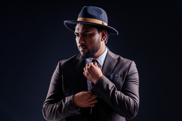 indian business man wearing hat and classic suit on black background in studio