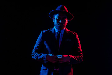 Young handsome model posing in a studio in a trendy neon light in a stylish suit and hat