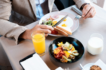 Cropped view of businessman sitting at served table and holding knife and fork in cafe