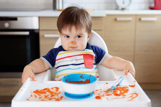 Cute messy baby in high chair with funny face