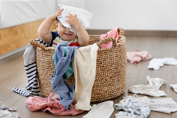 Funny baby sitting in laundry basket with clothes on head