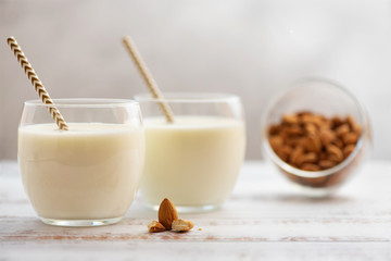 Almond milk in glasses with almond on a light wooden table