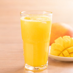 Fresh mango juice with beautiful chopped pulp flesh on bright wooden table background. Tropical fruit drink design concept. Close up, copy space.