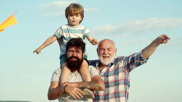 Father son and grandfather playing - family time together. Three men generation. Kid pilot with toy jetpack against sky background. Cute child hugging his father and grandfather.