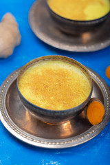Golden turmeric milk on the blue background with ingredients