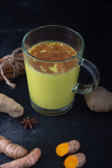 Golden turmeric milk on the black background with ingredients