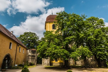 Fototapeta na wymiar Panensky Tynec, Czech Republic - July 15 2019: Yellow bell tower and stone gateway, as a part of the unfinished Gothic church of the Virgin Mary from 14th century. Sunny summer day with blue sky.