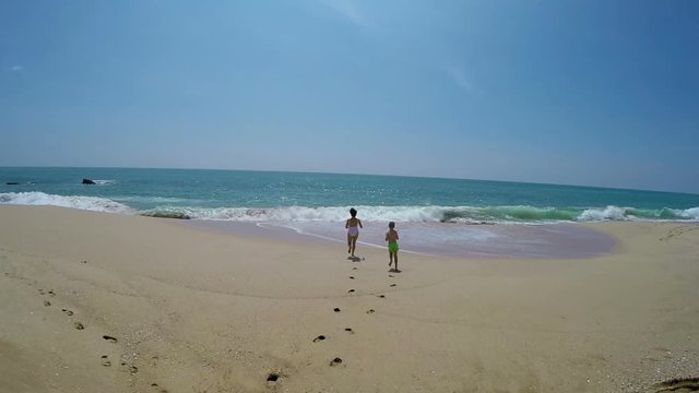 Son and mum running toward sea by sandy beach on clear day