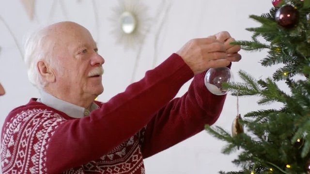 Medium shot of happy elderly couple smiling and decorating Christmas tree together