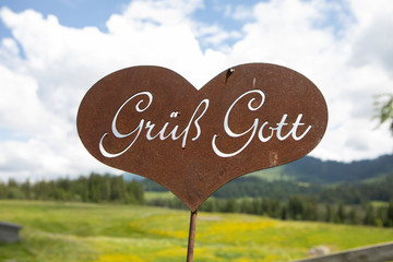 rusty welcome sign with german letters in the shape of a heart in an alpine pasture