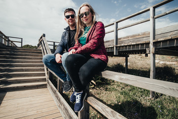 Couple in love sitting on stairs near ocean. Attractive pair enjoying ocean view on wooden path....