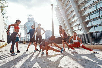 Full length of people in sports clothing warming up and stretching while exercising outdoors