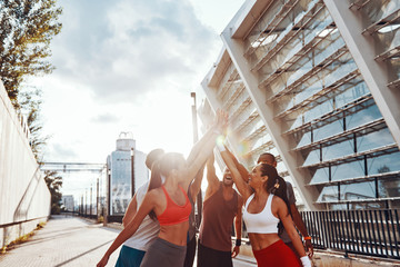 Group of young people in sports clothing holding hands together while standing outdoors