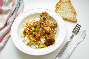 Chicken curry with rice one a white plate. Slices of bread, fork and knife.
