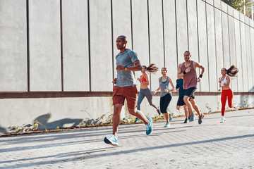 Full length of young people in sports clothing jogging while exercising on the sidewalk outdoors
