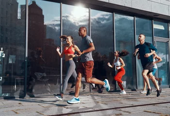 Foto op Plexiglas Full length of young people in sports clothing jogging while exercising on the sidewalk outdoors © gstockstudio