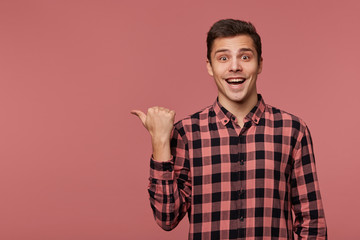 Young attractive cheerful man wears in checkered shirt, looks at the camera with happy expression,...