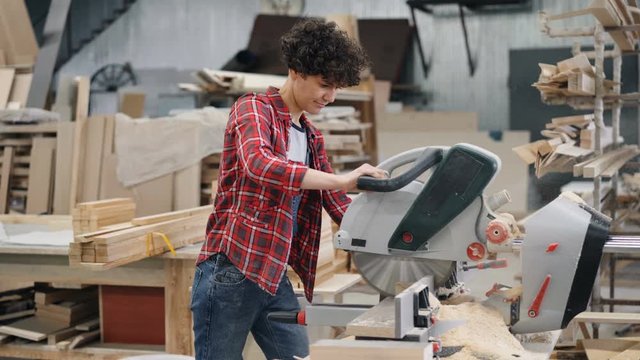 Beautiful young girl sawing timber with circular saw in wood workshop working alone cutting wooden plank then looking at woodware. People and job concept.