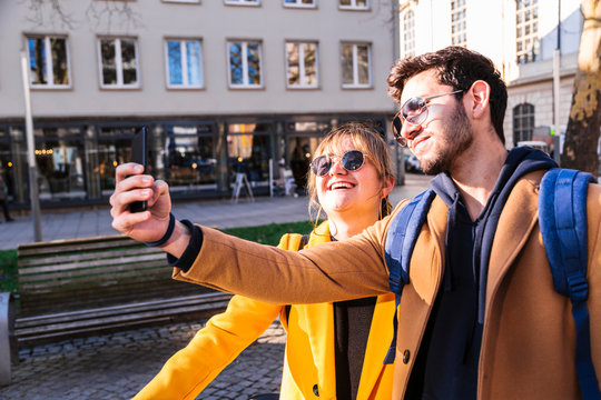 Happy couple in light coats taking selfie outdoors