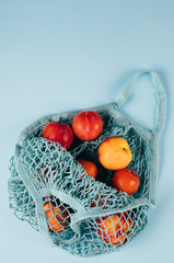Mesh shopping bag with fruits plims and peach on blue background. Top view, flat lay, copy space. Zero waste, eco friendly concept.