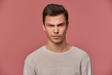 Fototapeta premium Close up of young handsome strict guy wears in basic long sleeve, looks at the camera with angry expression, isolated over pink background.