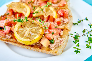 Appetizer bruschetta with tuna and tomatoes in white plate on blue background. Italian cuisine. Delicious Italian antipasti crostini. Copy space.