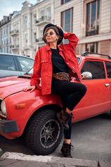 Fototapeta na wymiar Beautiful girl in a red jacket and sunglasses posing near a red car