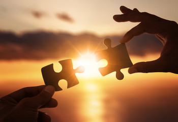Business concept. Close up of hands connecting two pieces of jigsaw puzzle over the beautiful sunset