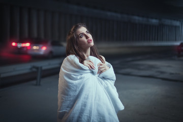 Woman wrapped herself in a blanket, she stands in a tunnel and looks up thoughtfully.