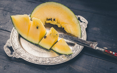 Slice yellow watermelon on a silver plate and knife on a dark wooden background