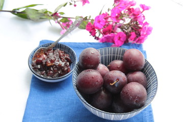 Ripe plums, jam, pink phlox flower on blue and white background