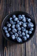 Handful blueberry berries in a black bowl on wooden brown table. Vitamin C and antioxidants- healthy diet food. Vertical.